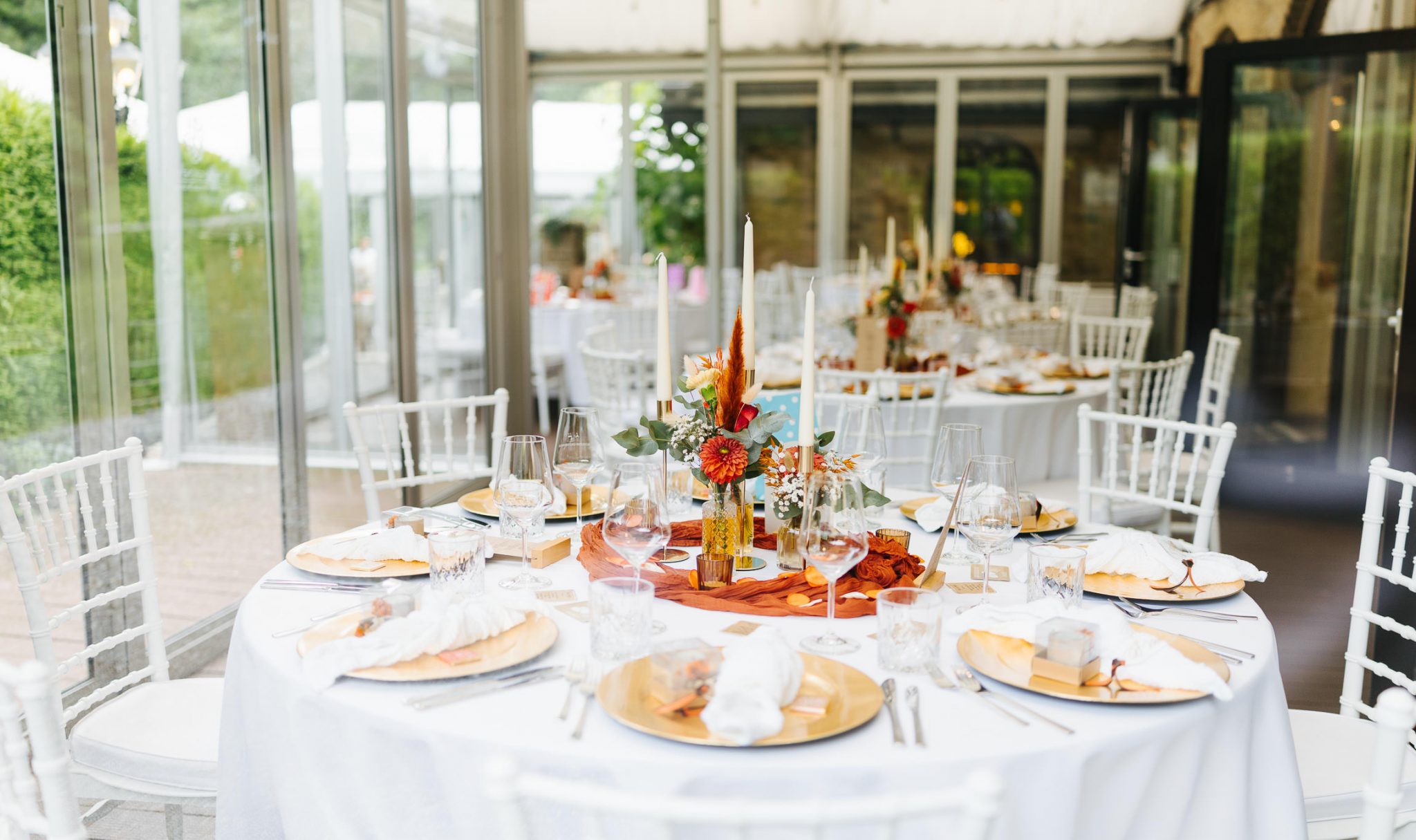 Festlich gedeckter Hochzeitstisch im Wintergarten von Schloss Grünewald in Solingen mit Kerzen, Blumen und goldenen Tellern.