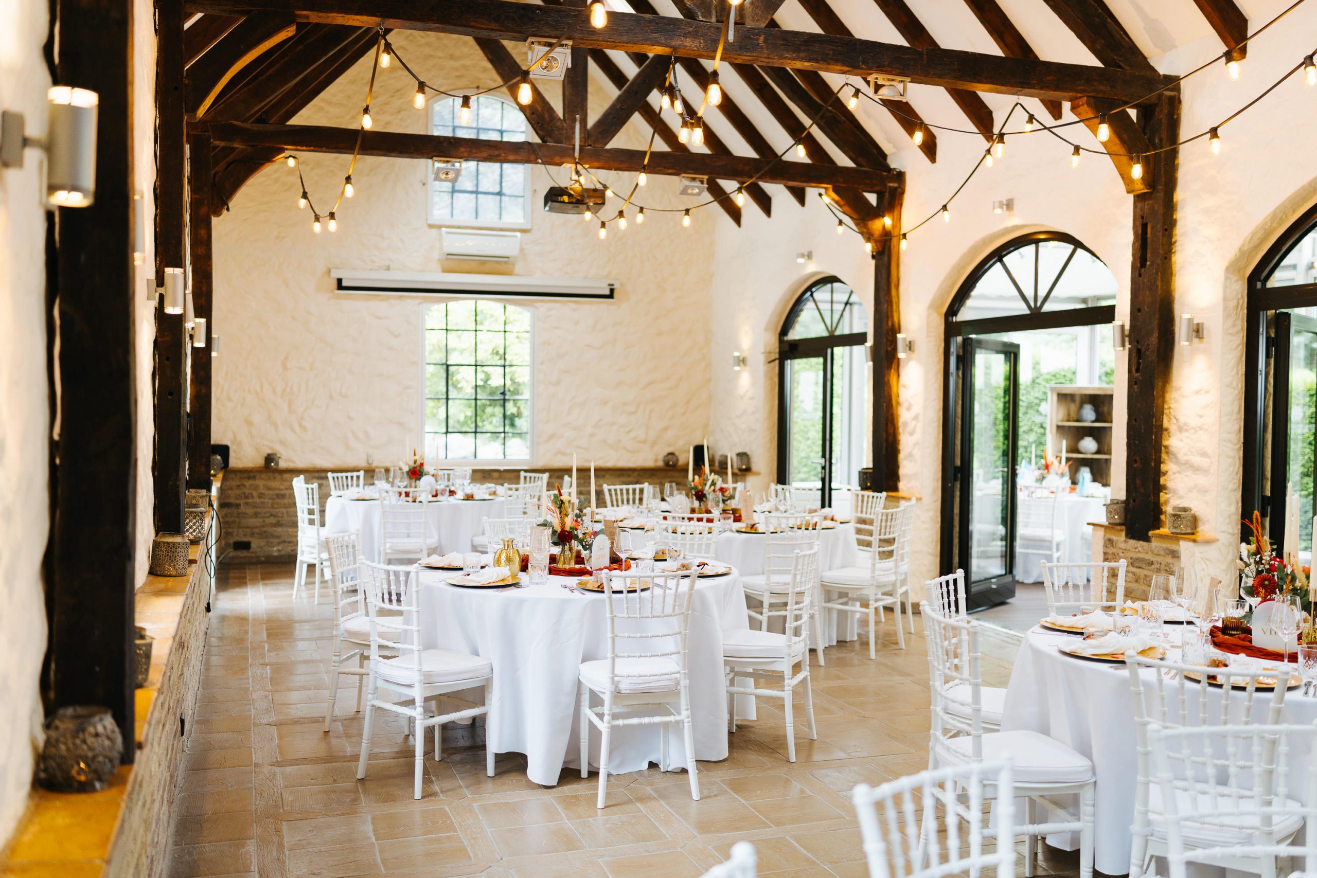 Hochzeitstafel im Festsaal von Schloss Grünewald mit weißen runden Tischen, Stühlen und warmen Lichterketten.