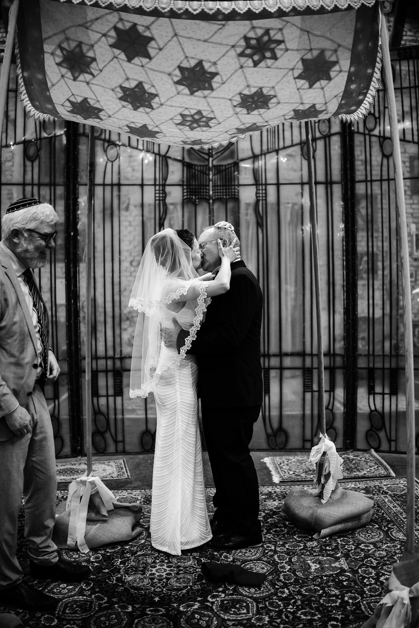Braut und Bräutigam küssen sich unter der Chuppa bei einer jüdischen Hochzeit im Gare du Neuss